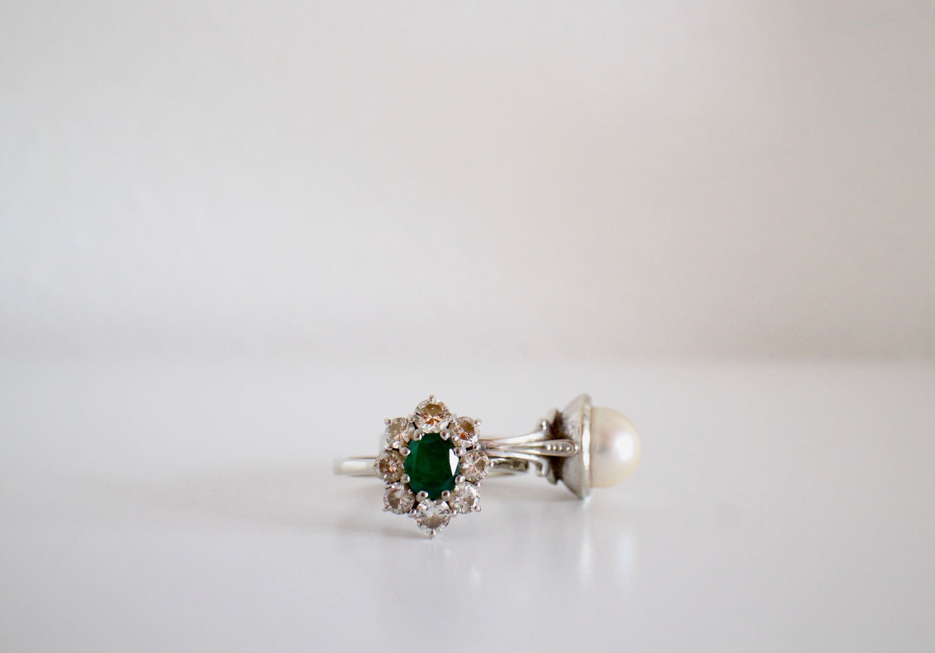 Witgouden ring met smaragd en briljant naast een ring met parel