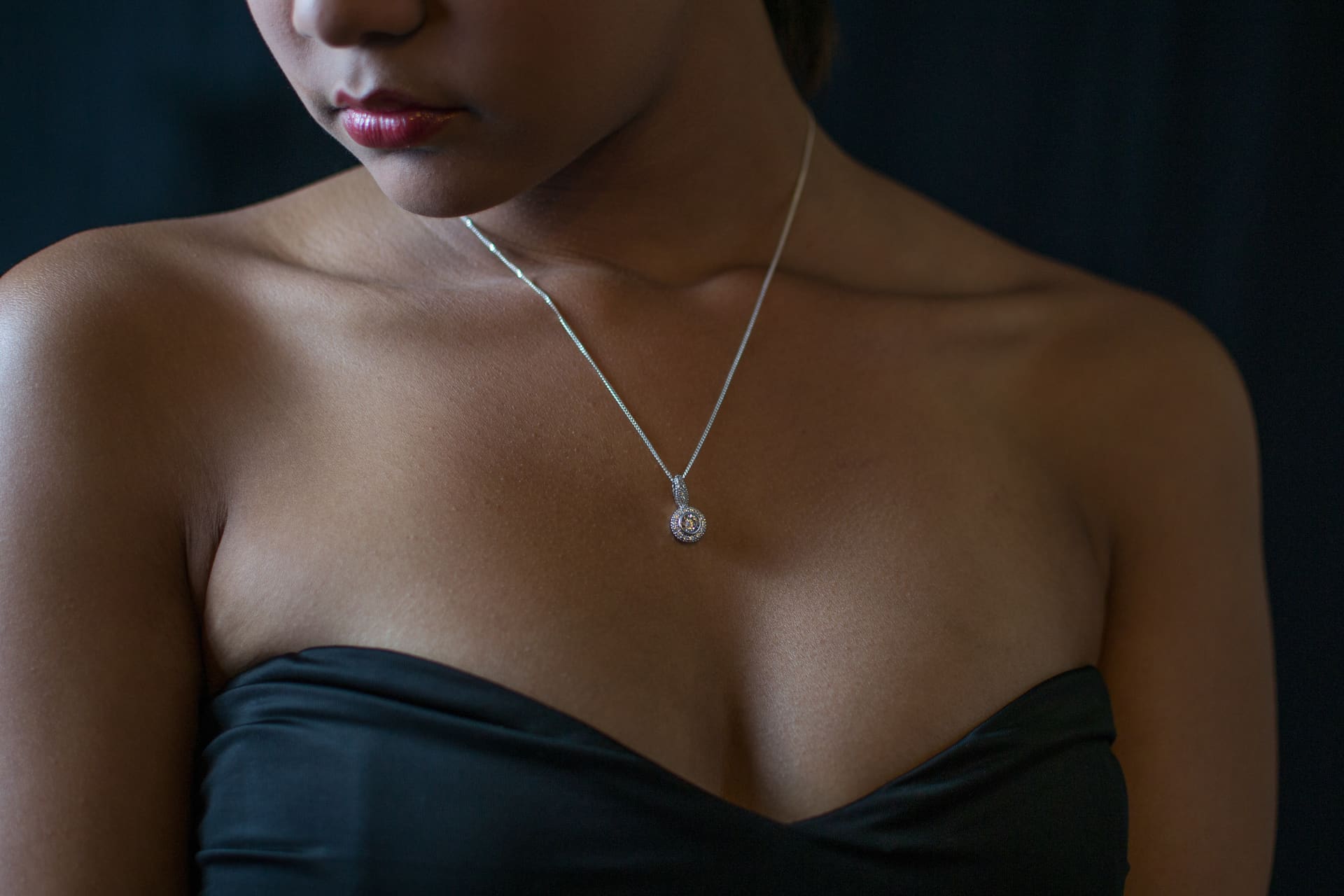 Zilveren collier met hanger om de hals van een vrouw in een zwarte jurk